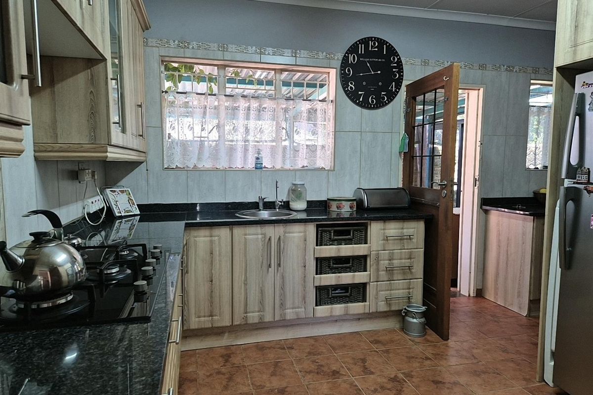 Functional kitchen featuring wood-look cabinetry, dark granite countertops, a built-in gas hob, and tiled flooring with direct access to an adjacent room.