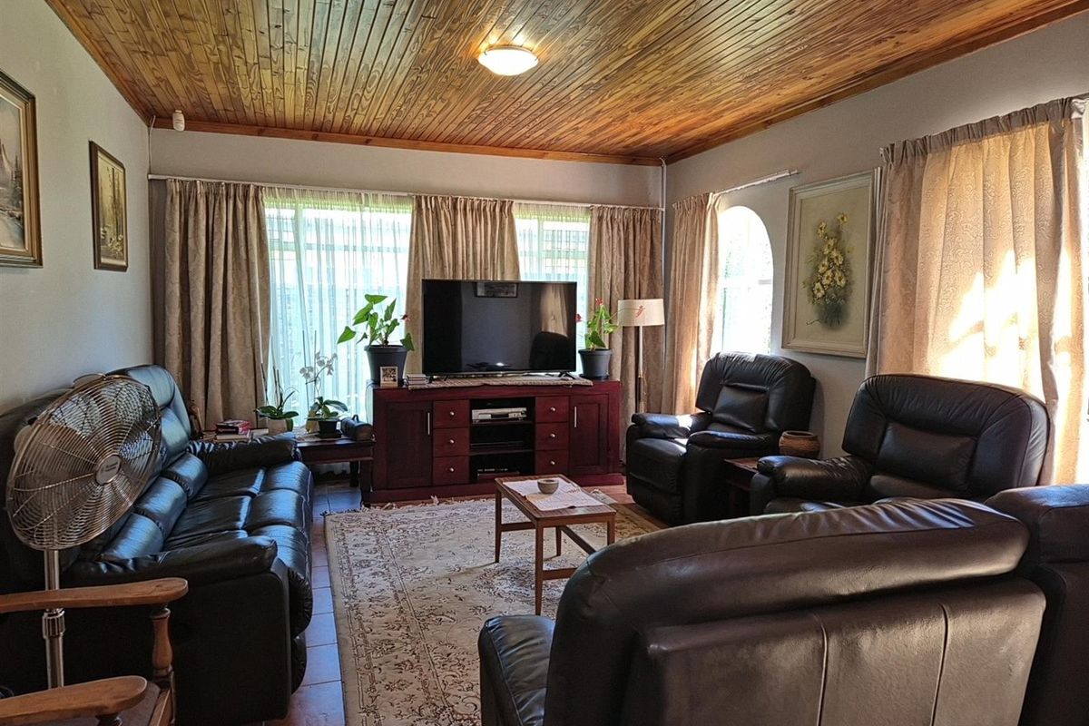 A comfortable living room featuring a distinctive timber-clad ceiling, tiled flooring, and large windows that provide ample natural light.
