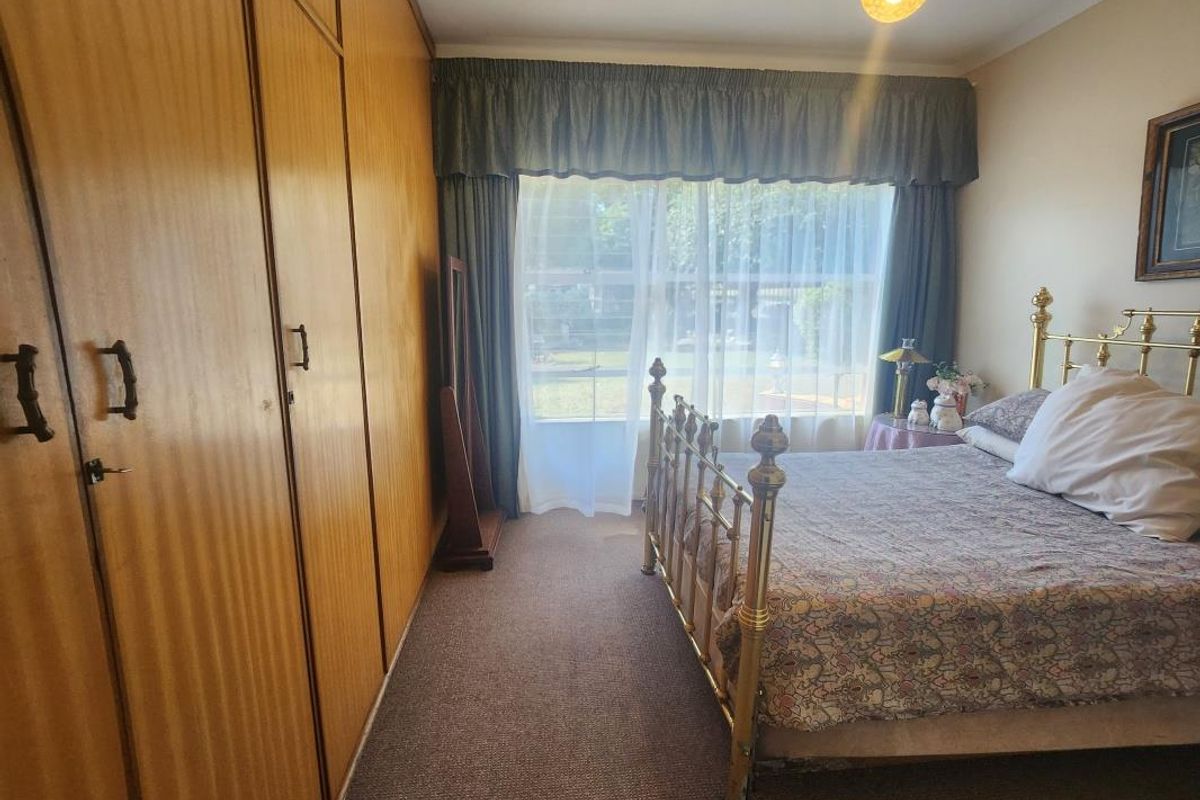 A bedroom featuring wall-to-wall built-in wooden cupboards and carpeted flooring, offering a functional layout with natural light.