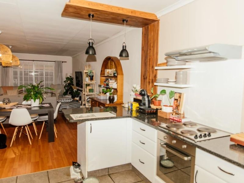 Open-plan kitchen and living area featuring granite countertops, built-in oven, electric hob, and a decorative timber bulkhead, creating a functional and connected living space.