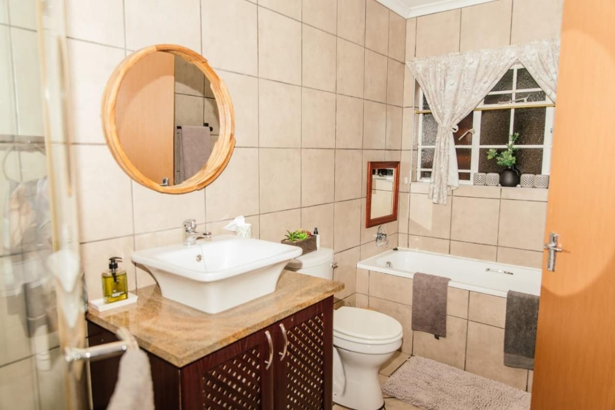 A functional bathroom featuring a vanity with a vessel sink, a built-in bathtub, a toilet, and a glass-enclosed shower with neutral wall tiling.