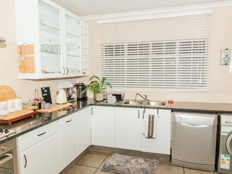 A functional kitchen featuring white cabinetry, granite countertops, a double basin sink, and integrated appliances, complemented by tiled flooring and natural light.