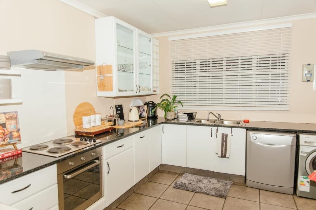 Functional kitchen featuring white cabinetry, granite countertops, stainless steel oven, electric hob, extractor fan, and tiled flooring with ample natural light.