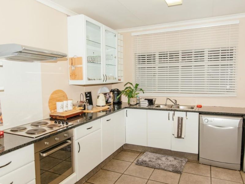 Functional kitchen featuring white cabinetry, granite countertops, stainless steel oven, electric hob, extractor fan, and tiled flooring with ample natural light.