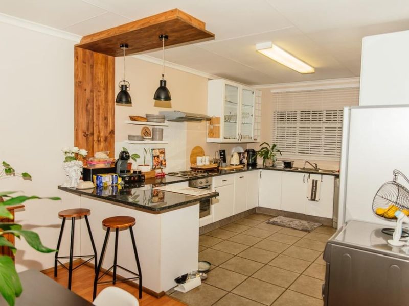 A functional kitchen featuring granite countertops, built-in oven and hob, tiled flooring, and a unique wooden breakfast bar feature with pendant lighting.