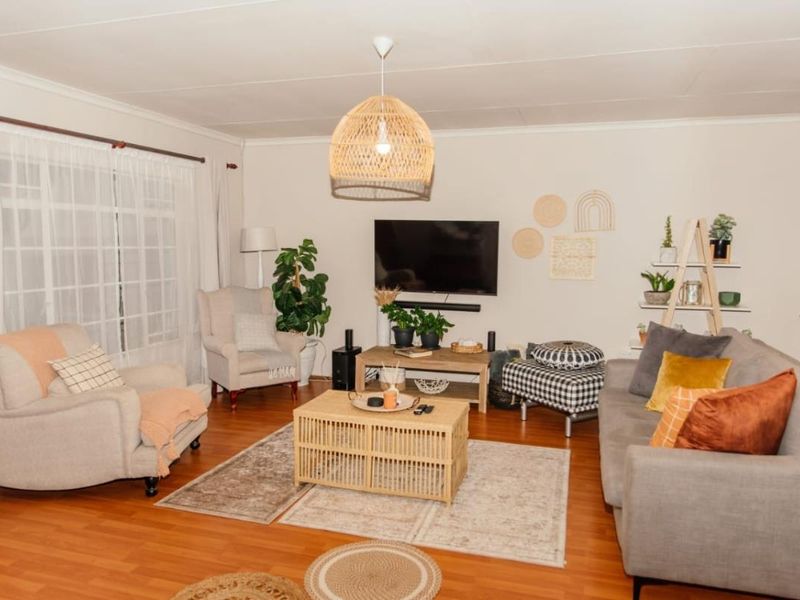 A well-lit living room featuring laminate flooring, a large sliding glass door for natural light, and a central pendant light fixture.
