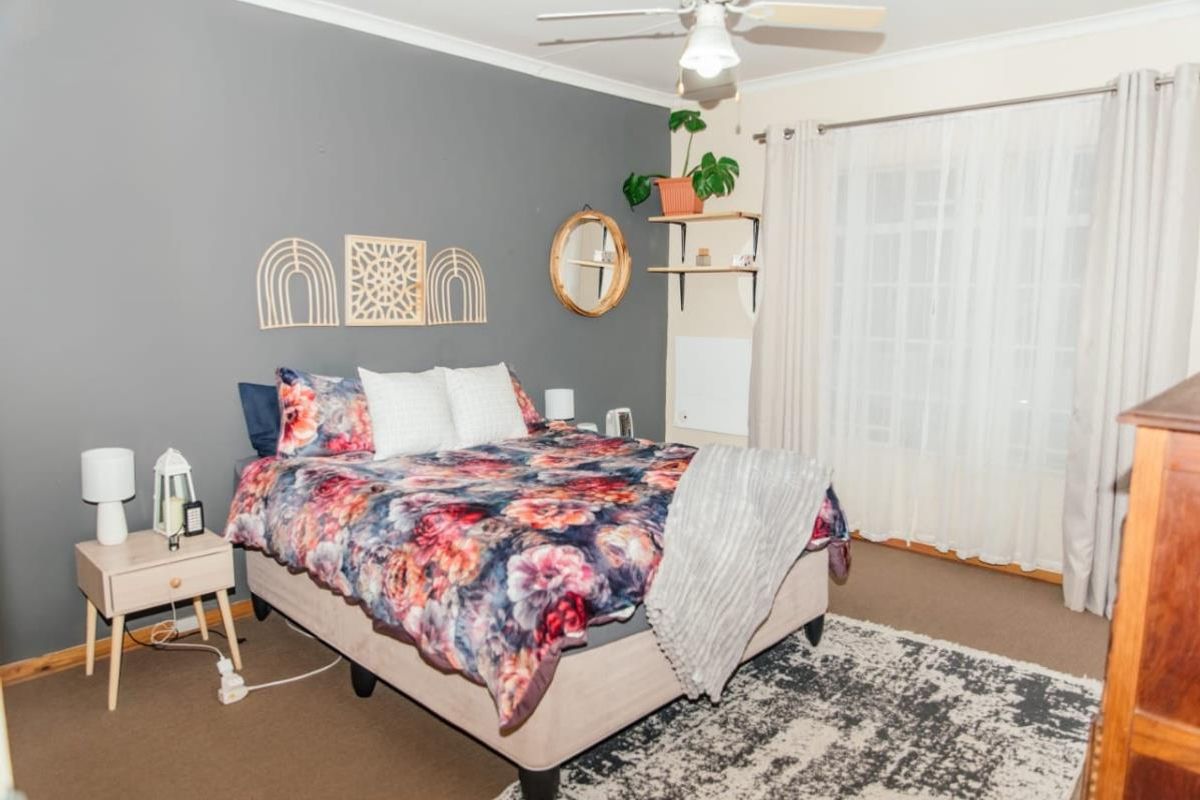 A bedroom featuring carpeted flooring, a ceiling fan, and large windows with curtain tracks, providing a functional and comfortable living space.