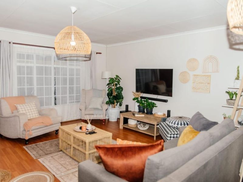 A well-maintained living room featuring laminate flooring, a large window with curtain rails, and a central pendant light fixture.