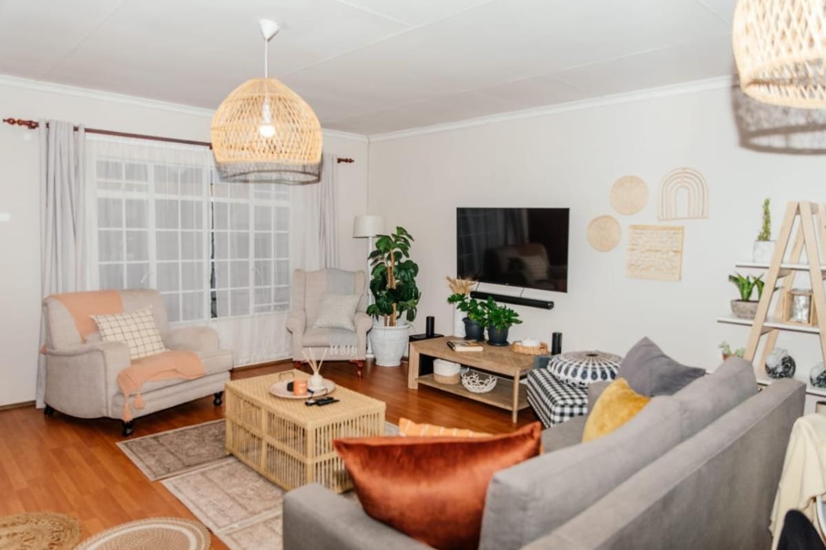 A well-maintained living room featuring laminate flooring, a large window with curtain rails, and a central pendant light fixture.