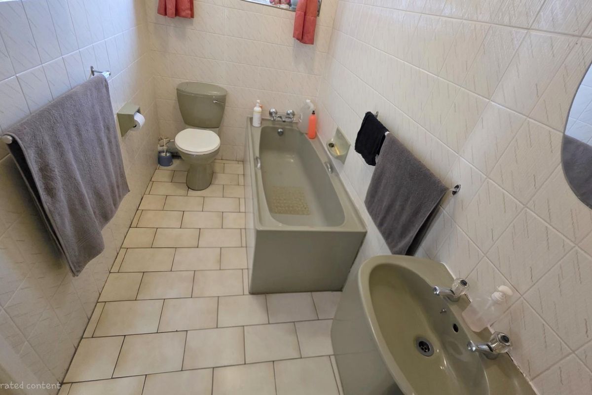A dated bathroom featuring a full-size bathtub, pedestal basin, and toilet with neutral wall tiling and floor tiles.