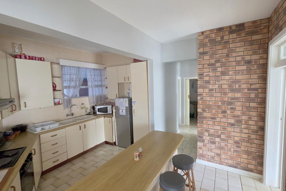 A functional kitchen featuring cream-colored cabinetry, a built-in hob and extractor fan, and a distinctive exposed brick feature wall.