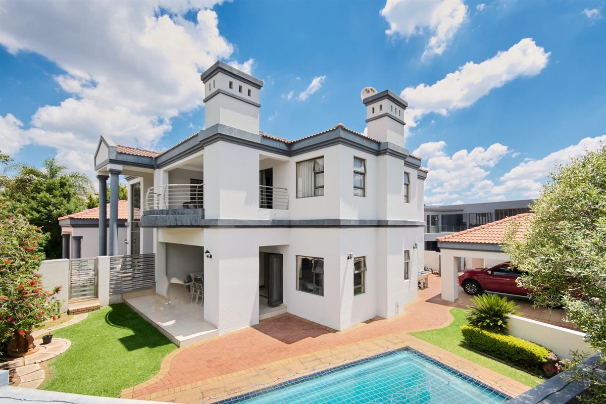 Rear view of a two-story house featuring a swimming pool, covered patio, balcony, and a paved garden area with a carport.