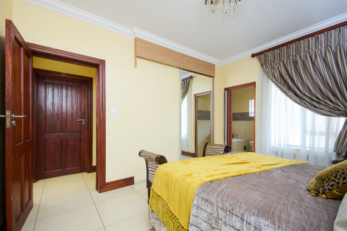 A bedroom featuring tiled flooring, crown molding, and a built-in mirrored wardrobe with direct access to an en-suite bathroom.