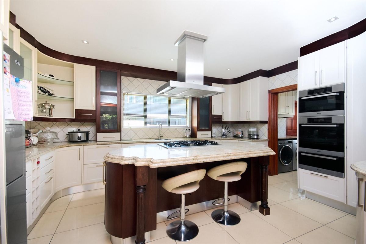 Spacious kitchen featuring a central island with a gas hob, stone countertops, built-in double ovens, and ample cabinetry, with an adjacent scullery area.