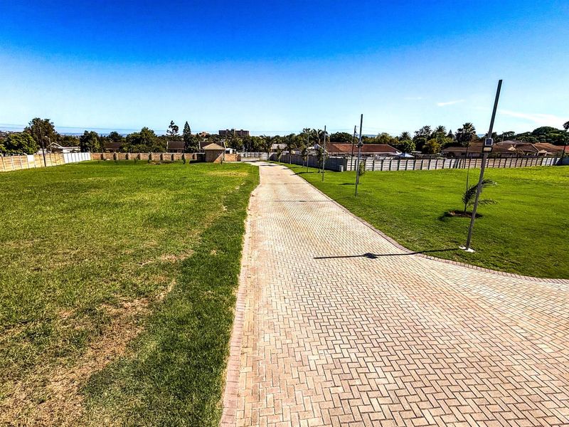 A wide, vacant residential plot featuring a paved driveway, manicured lawn, and perimeter boundary walls.