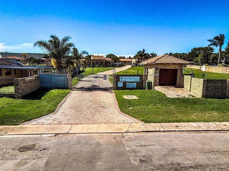 View of the entrance to Vanes Estate Gardens, featuring a paved driveway, security gate, brick boundary walls, and a small guardhouse structure.