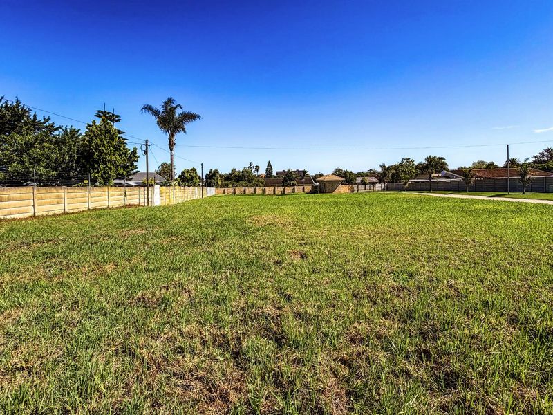 A vacant residential plot featuring level grass terrain, enclosed by perimeter boundary walls, and situated in an established neighborhood setting.