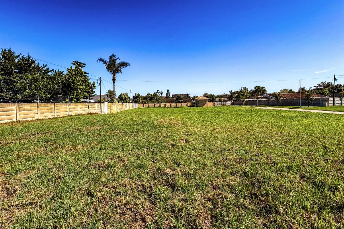A vacant residential plot featuring level grass terrain, enclosed by perimeter boundary walls, and situated in an established neighborhood setting.