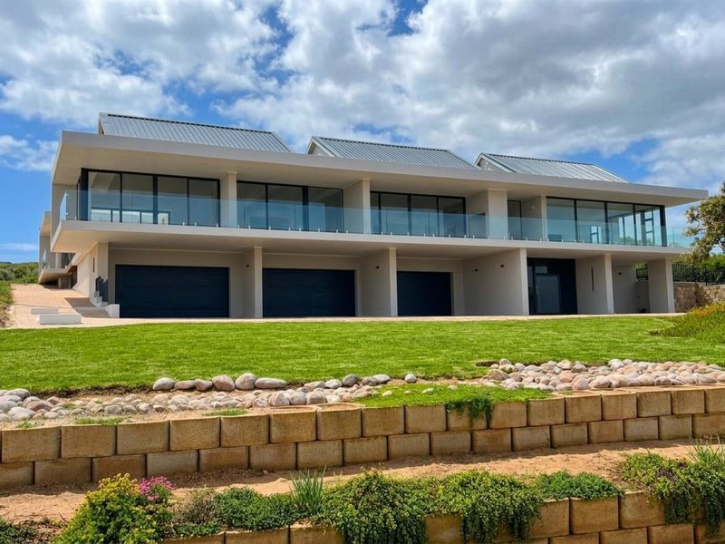 Modern multi-level residence featuring a triple garage, expansive upper-level balcony with glass balustrades, and well-maintained landscaped grounds.