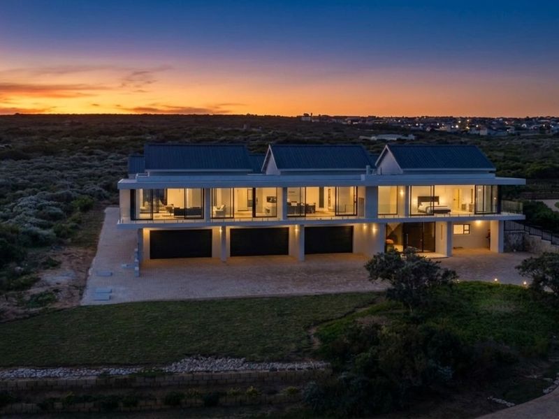 Stunning aerial view of a modern luxury residence at dusk, featuring a triple garage, expansive glass facade, and a spacious paved driveway.