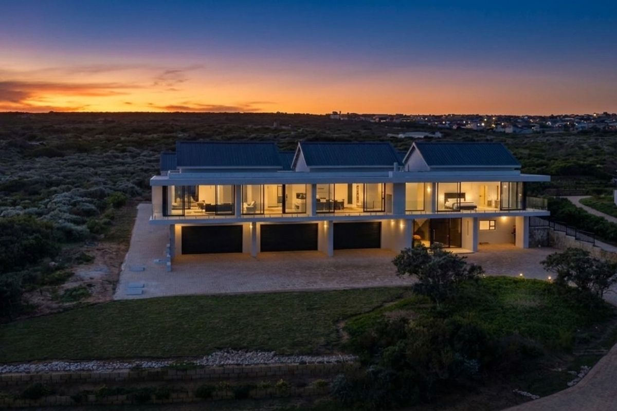 Stunning aerial view of a modern luxury residence at dusk, featuring a triple garage, expansive glass facade, and a spacious paved driveway.
