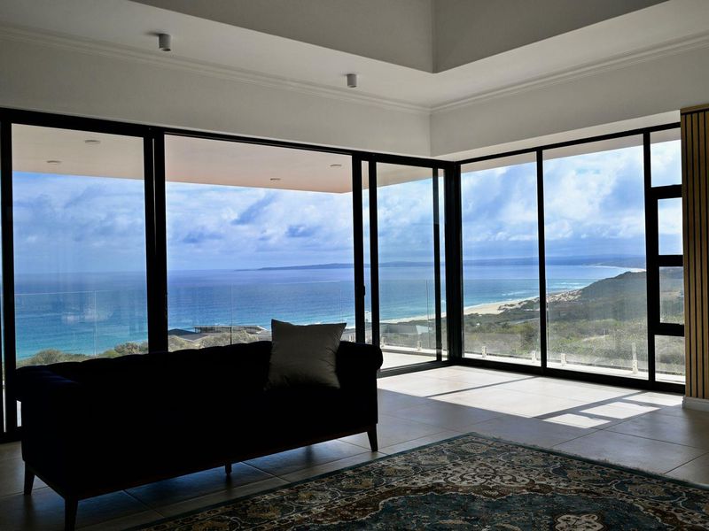 Spacious living area featuring expansive floor-to-ceiling sliding doors that frame panoramic ocean and coastal views, complemented by modern finishes and a recessed ceiling.