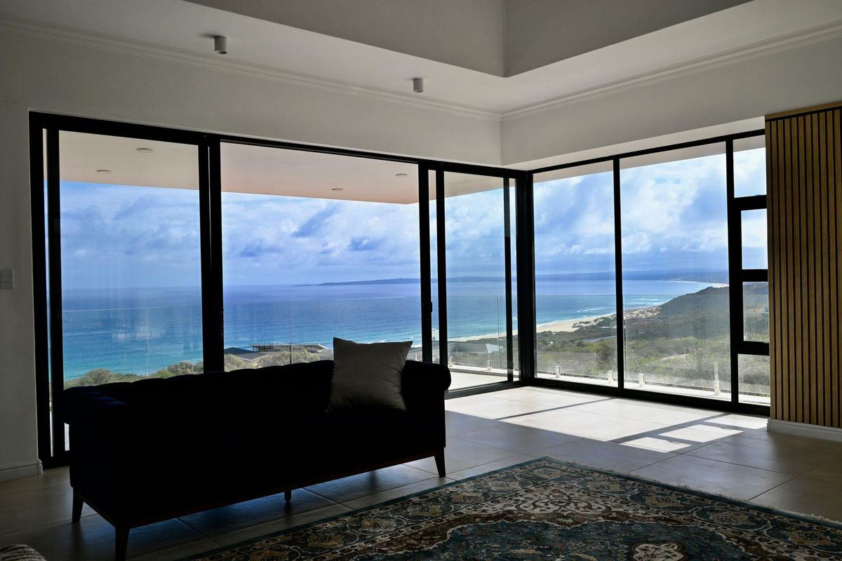 Spacious living area featuring expansive floor-to-ceiling sliding doors that frame panoramic ocean and coastal views, complemented by modern finishes and a recessed ceiling.