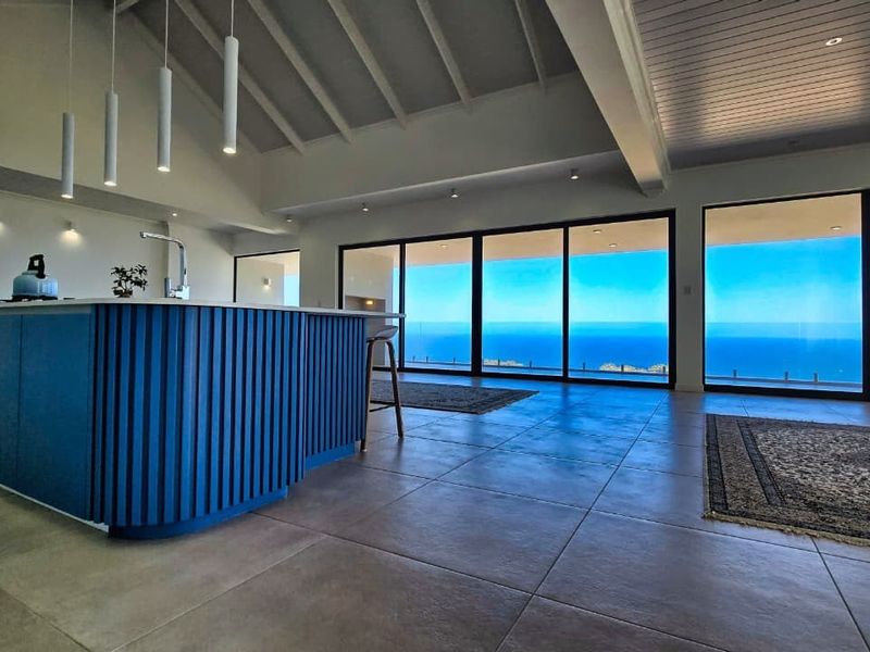 Spacious open-plan living and kitchen area featuring a modern blue island, vaulted ceilings, and expansive sliding doors offering panoramic ocean views.