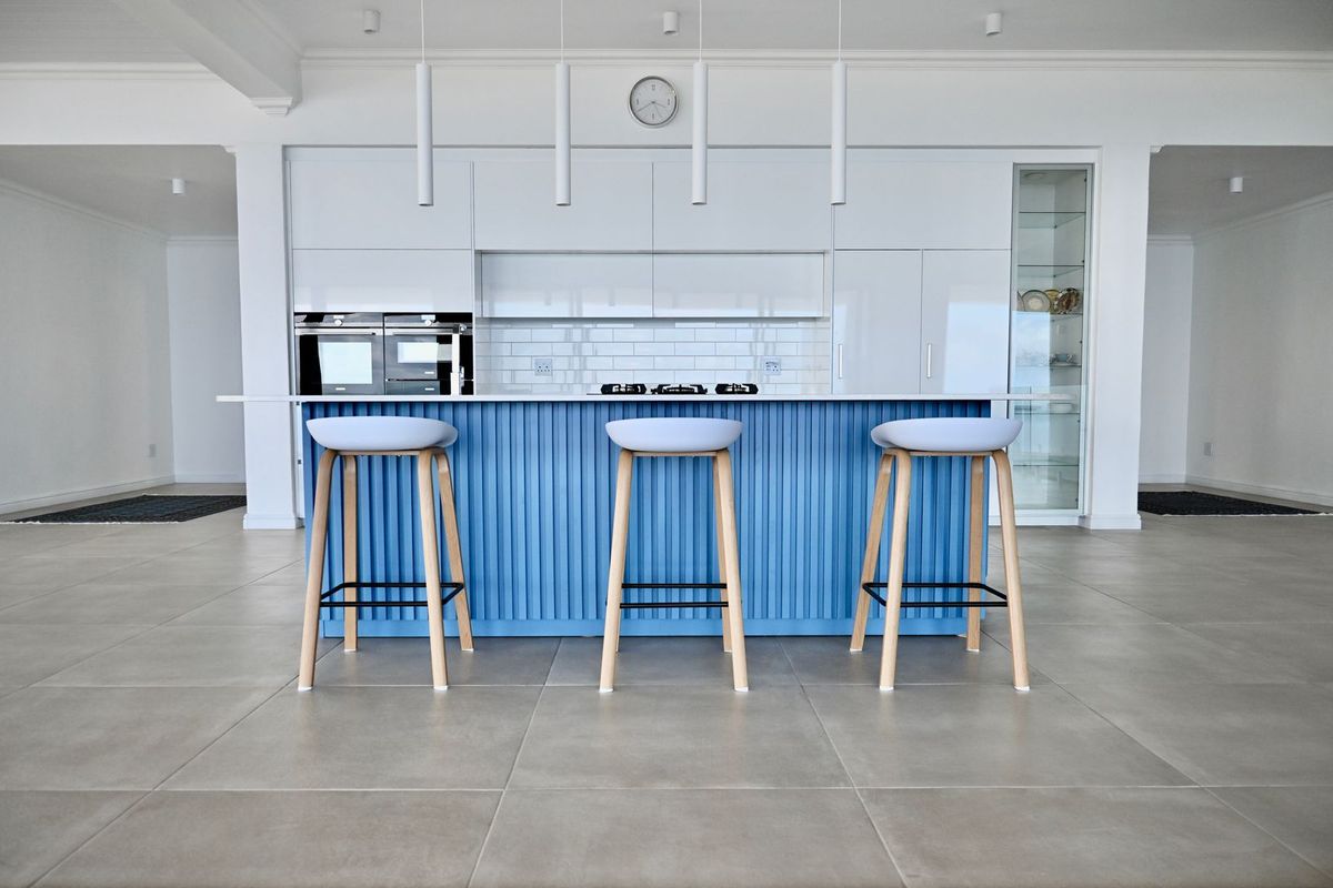 Modern kitchen featuring a blue island, white cabinetry, built-in oven, gas hob, and subway tile backsplash with sleek pendant lighting.