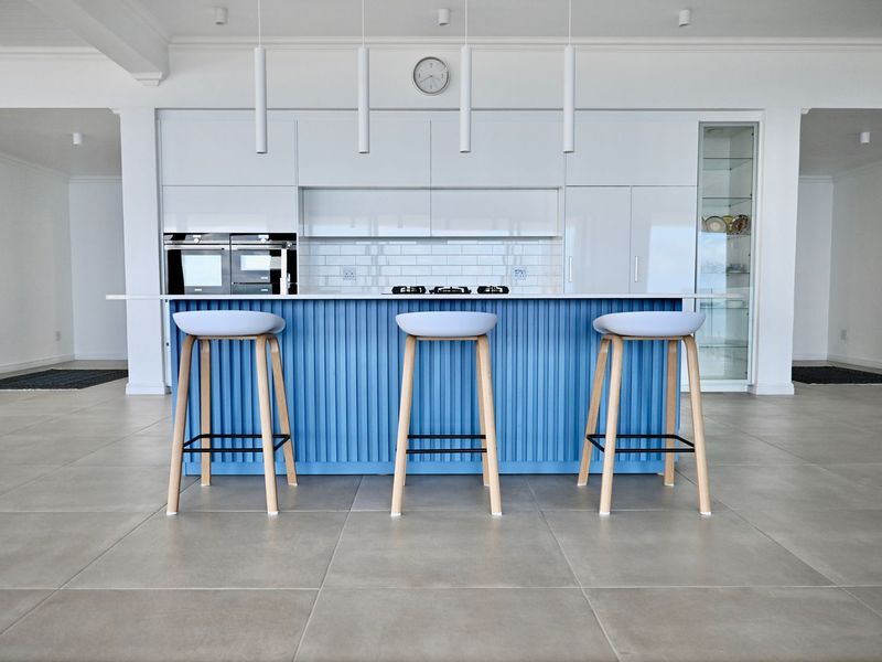 Modern kitchen featuring a blue island, white cabinetry, built-in oven, gas hob, and subway tile backsplash with sleek pendant lighting.