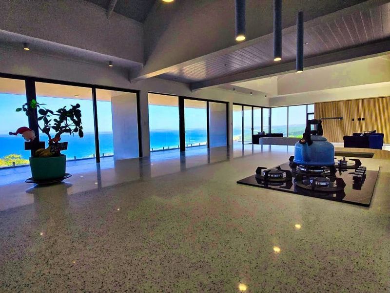 Spacious open-plan living area featuring a modern kitchen island with gas cooktop, high ceilings, and expansive sliding glass doors offering panoramic ocean views.