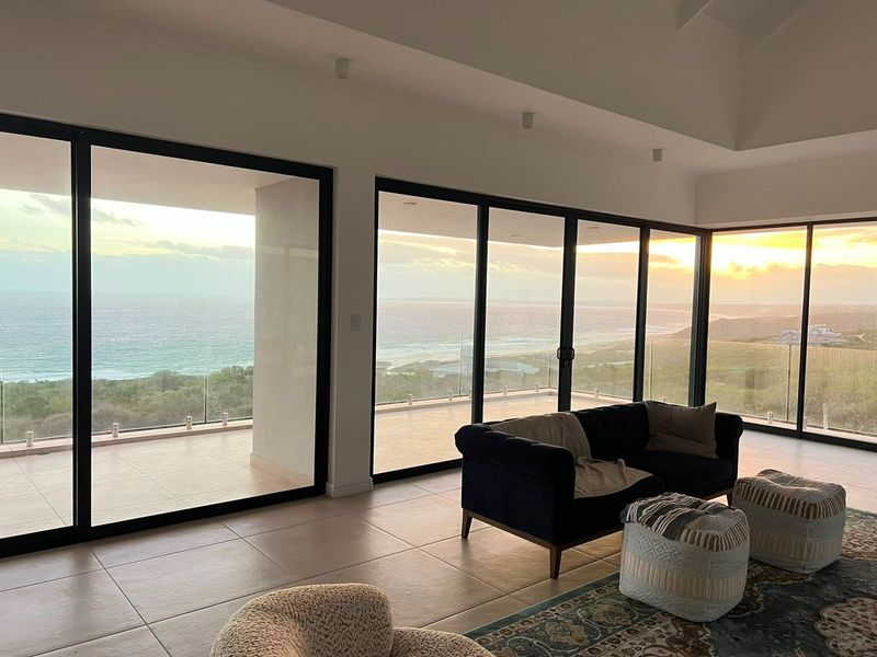 Spacious living area featuring large format floor tiles, vaulted ceilings, and expansive floor-to-ceiling sliding doors opening onto a balcony with panoramic ocean views.