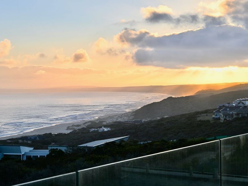 Stunning elevated coastal view overlooking the ocean and coastline at sunset, framed by a modern glass balustrade.