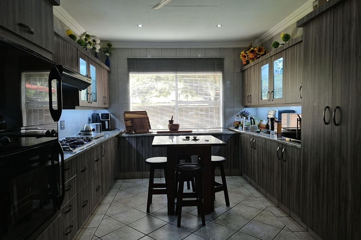 A well-appointed kitchen featuring dark wood-grain cabinetry, integrated oven and hob, tiled flooring, and a central breakfast nook with recessed ceiling lighting.
