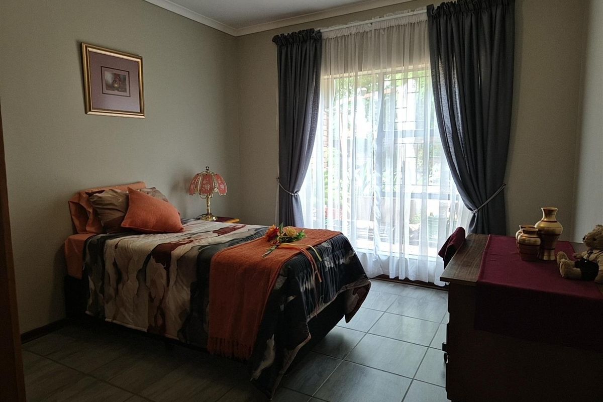 A well-lit bedroom featuring tiled flooring, a ceiling fan, and large windows with curtains providing natural light.