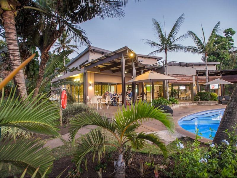 A well-maintained outdoor pool area featuring a paved deck, covered patio space, and direct access to the main residence through sliding glass doors.
