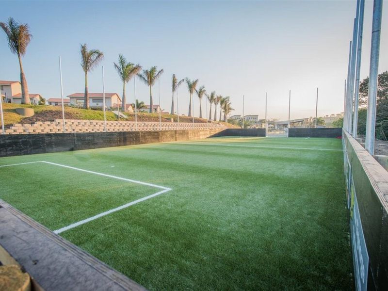 A well-maintained outdoor artificial turf sports field featuring perimeter fencing, goal posts, and tiered retaining walls.