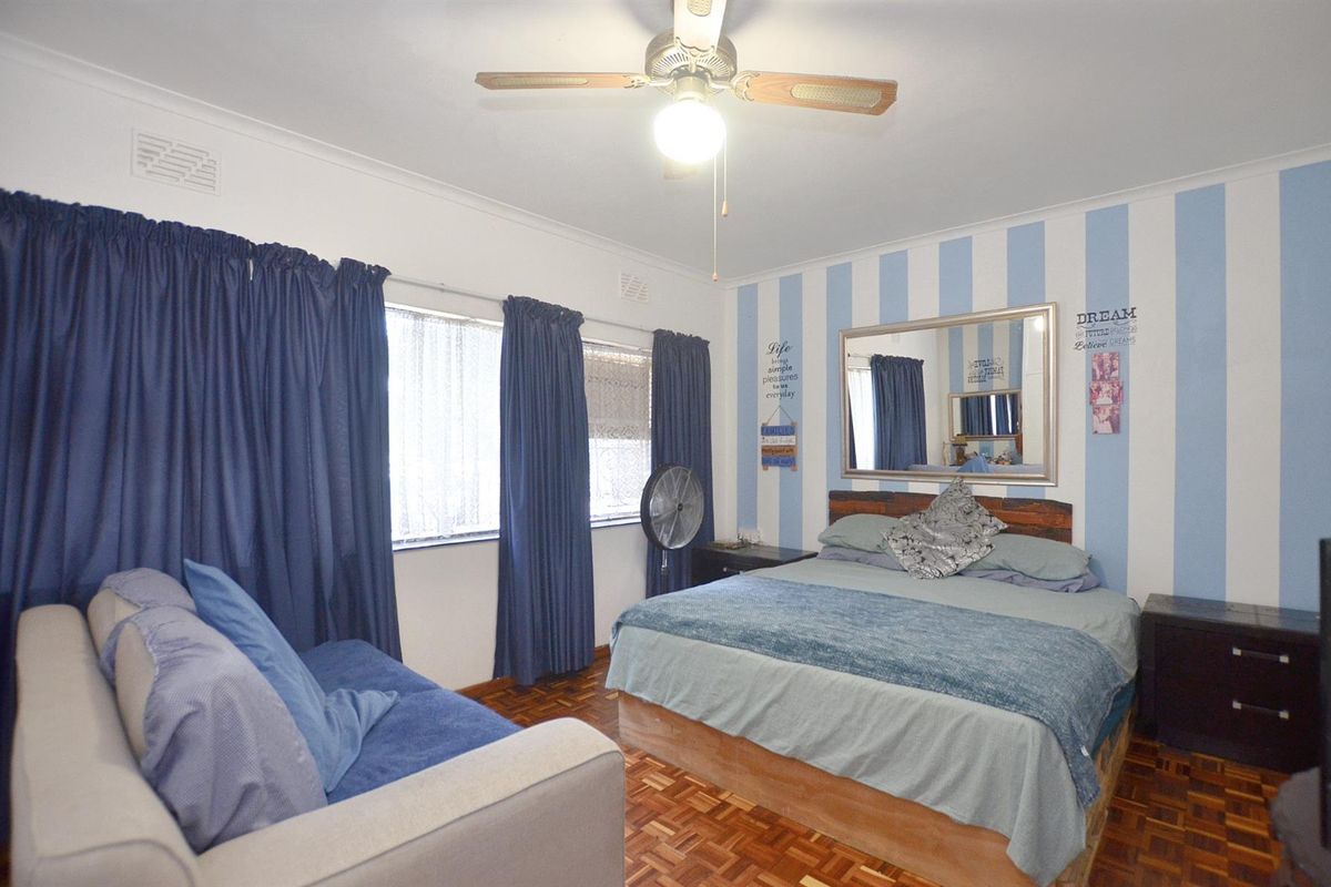A bedroom featuring parquet flooring, a ceiling fan, and large windows with curtains.