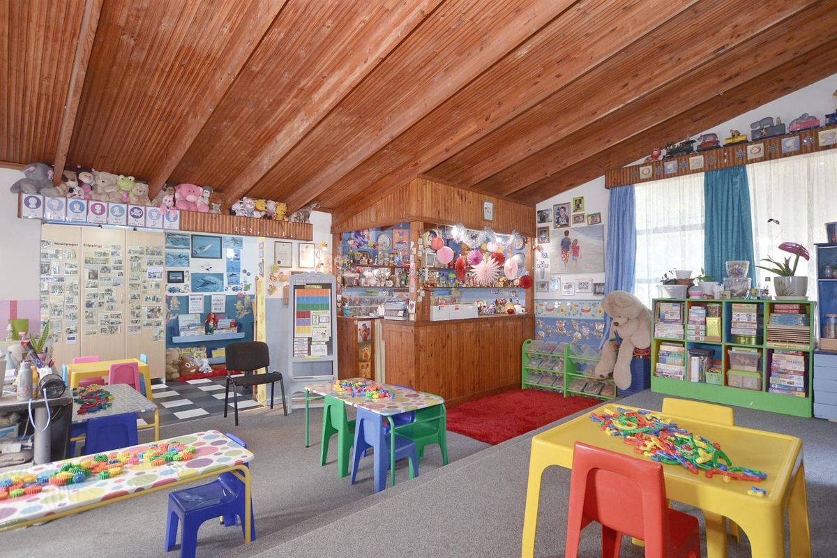 A spacious room featuring a high vaulted timber-clad ceiling and a built-in wooden service counter, currently utilized as a childcare or educational space.