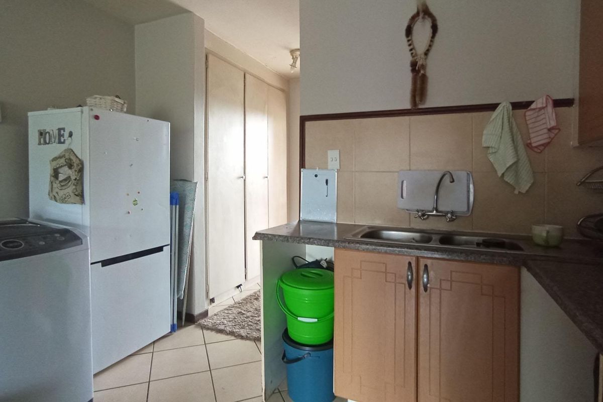 A functional kitchen area featuring built-in cabinetry, a double-basin sink, and tiled splashbacks, with adjacent space for laundry appliances.