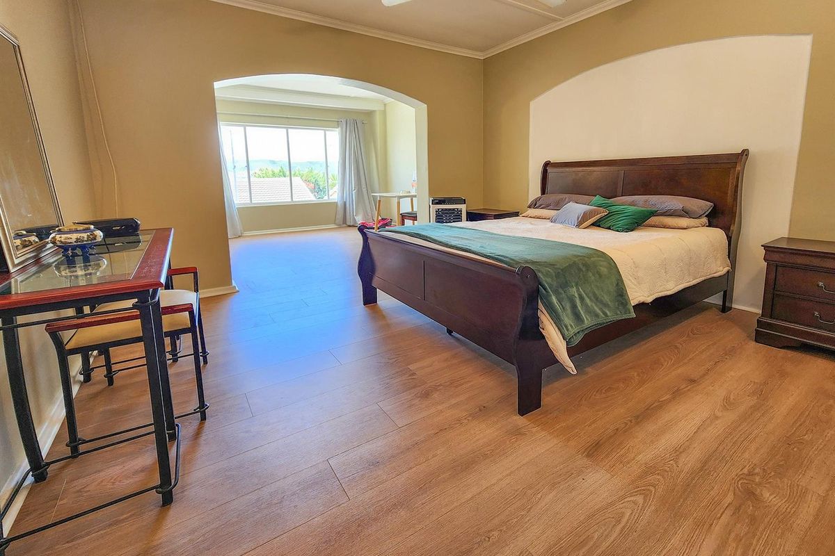 Spacious bedroom featuring wood-look flooring, a ceiling fan, and an adjoining sunroom area with large windows providing natural light and views.