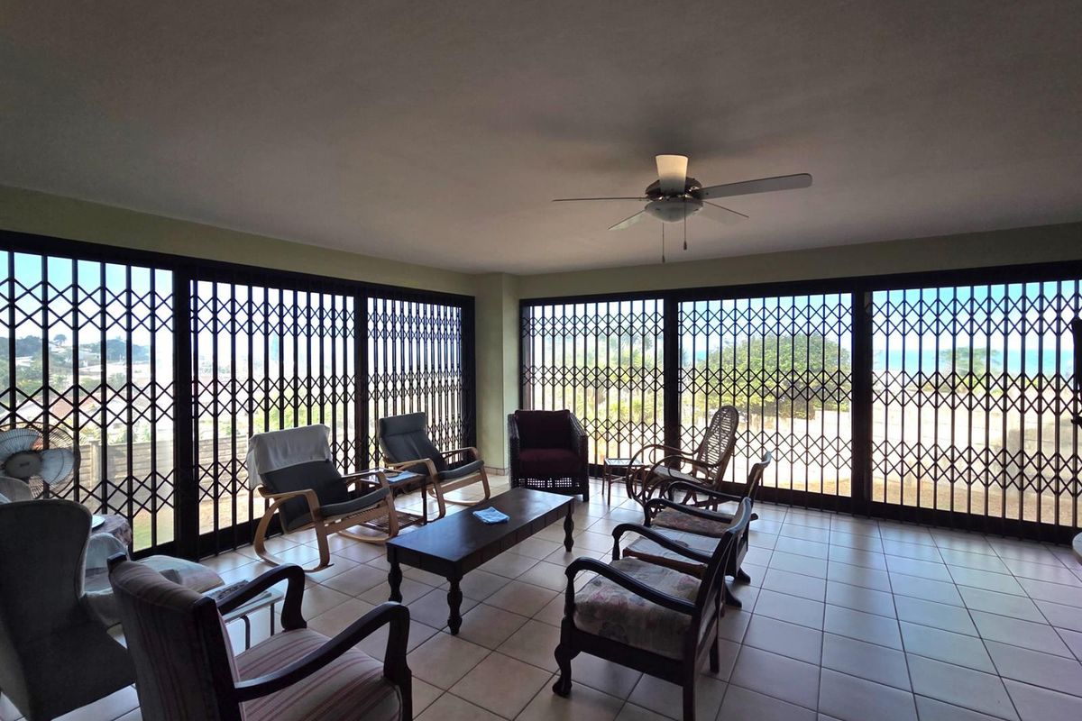 Spacious living area featuring large sliding glass doors with security gates, tiled flooring, and a ceiling fan, offering ample natural light.