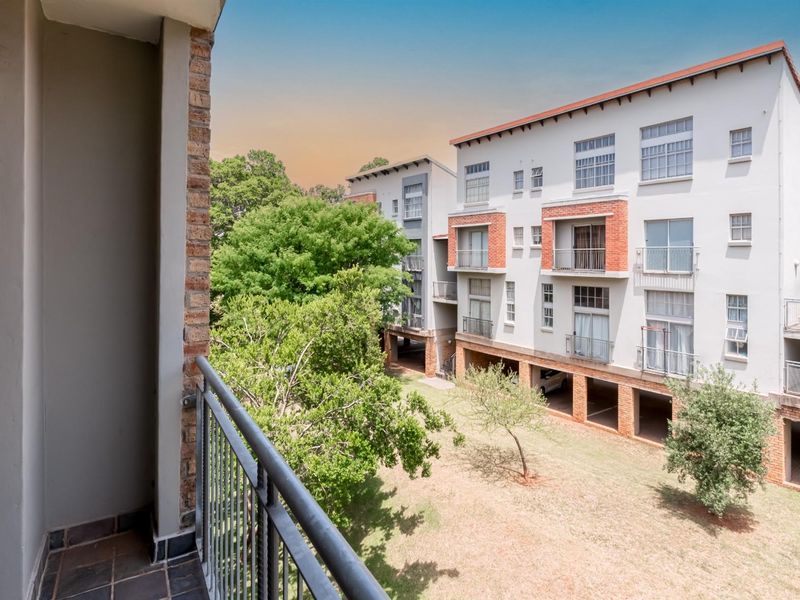 A private balcony with metal balustrades overlooking the apartment complex grounds and surrounding trees.