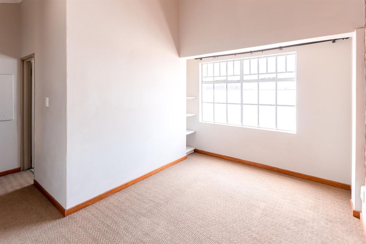 A bright, empty bedroom featuring neutral carpet flooring, built-in shelving, and a large multi-pane window allowing for natural light.