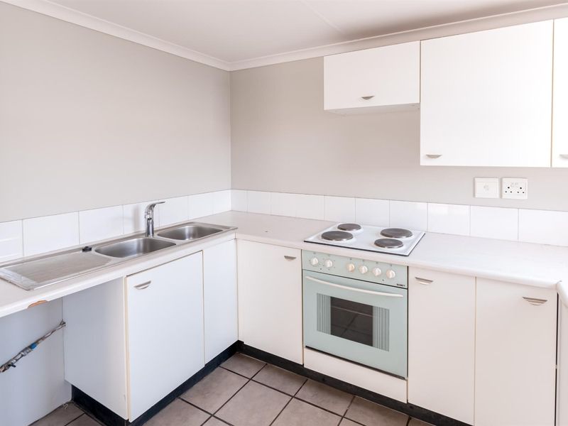 A functional kitchen featuring white built-in cabinetry, a stainless steel sink, and an integrated electric oven and hob with tiled splashbacks.