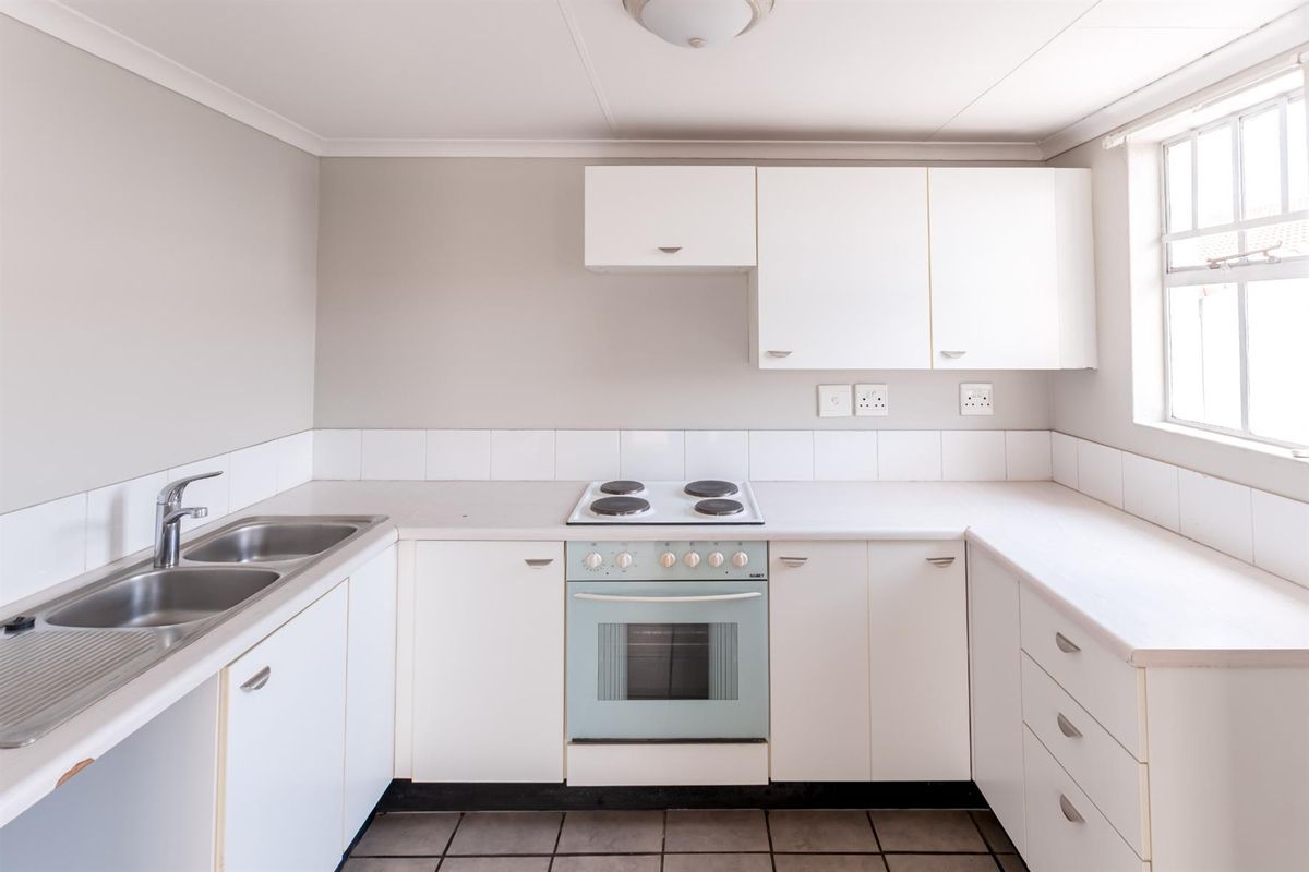 A functional, empty kitchen featuring white built-in cabinetry, laminate countertops, a double sink, and a built-in electric oven and hob.