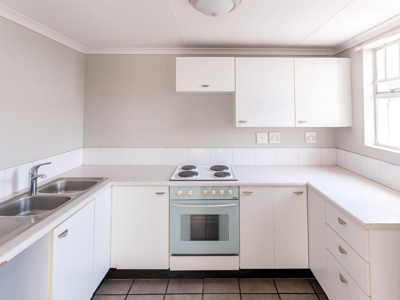 A functional, empty kitchen featuring white built-in cabinetry, laminate countertops, a double sink, and a built-in electric oven and hob.
