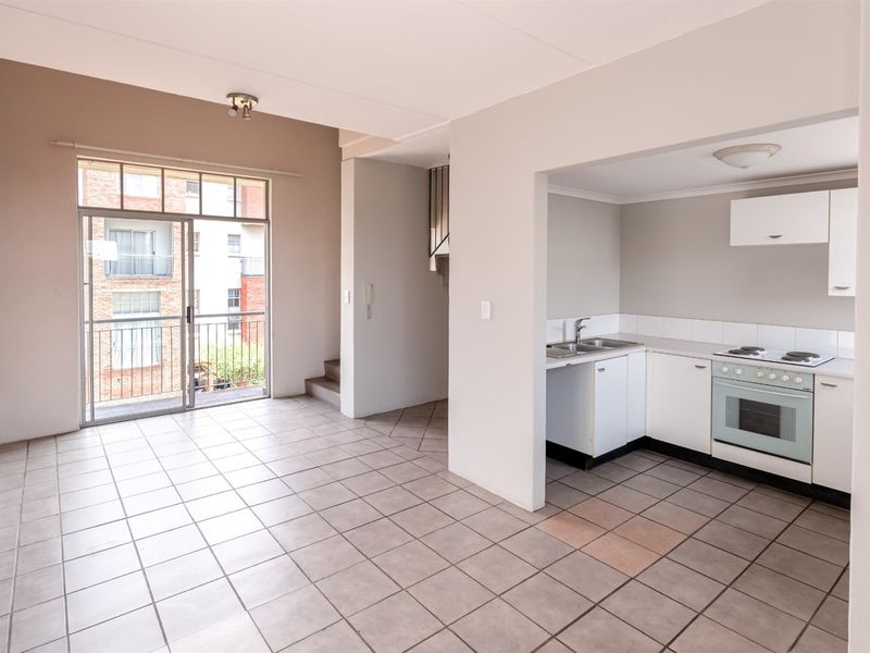 Open-plan living area featuring tiled floors, an exposed brick wall, and a functional kitchen with built-in cabinetry, leading to a balcony.