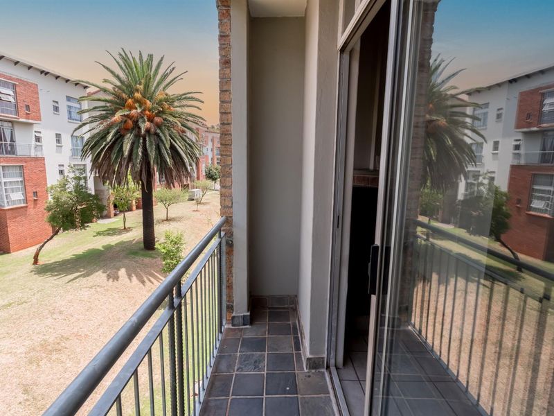 A private balcony featuring tiled flooring and a metal balustrade, offering views over the apartment complex grounds.