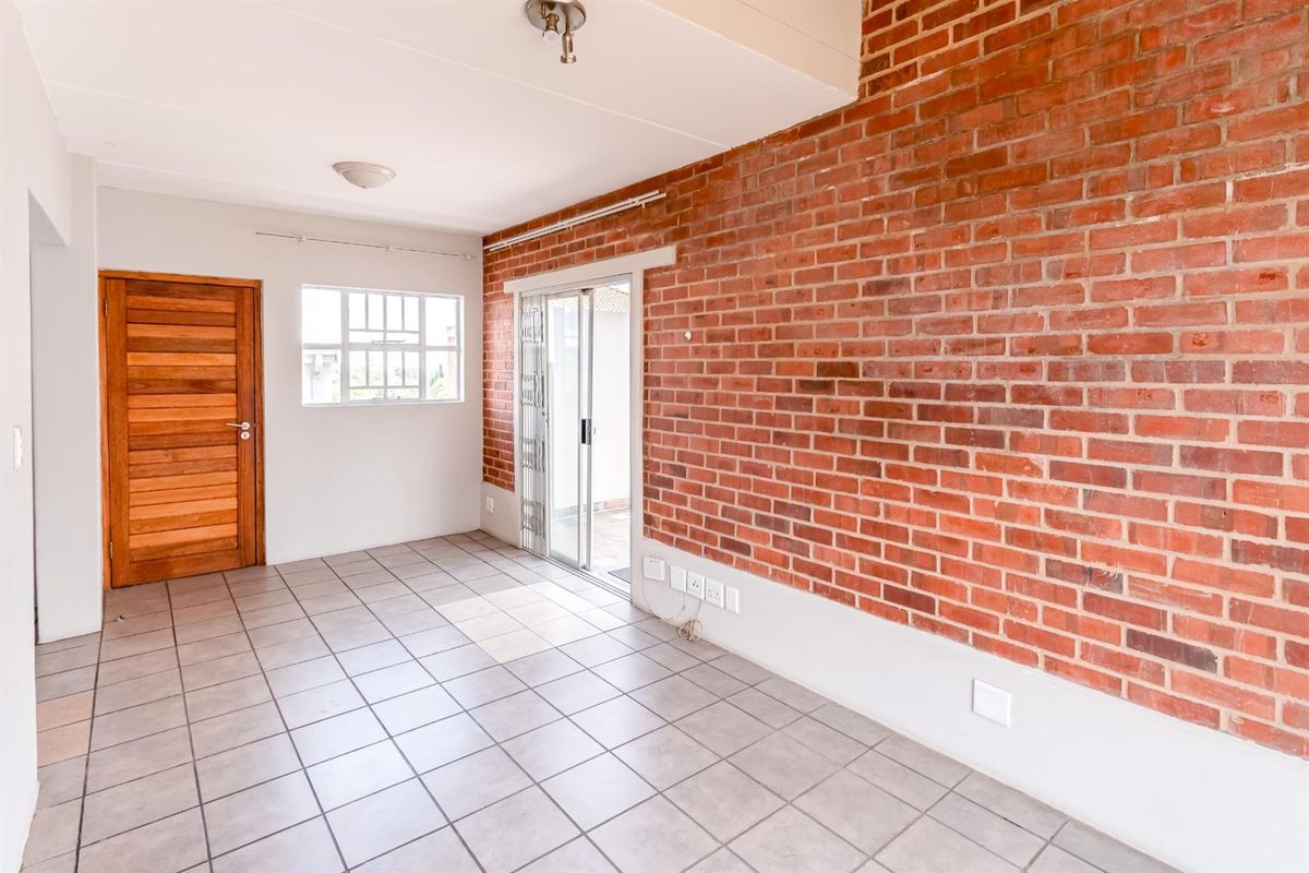 An empty living room featuring an exposed brick feature wall, tiled flooring, and a sliding glass door providing access to the exterior.